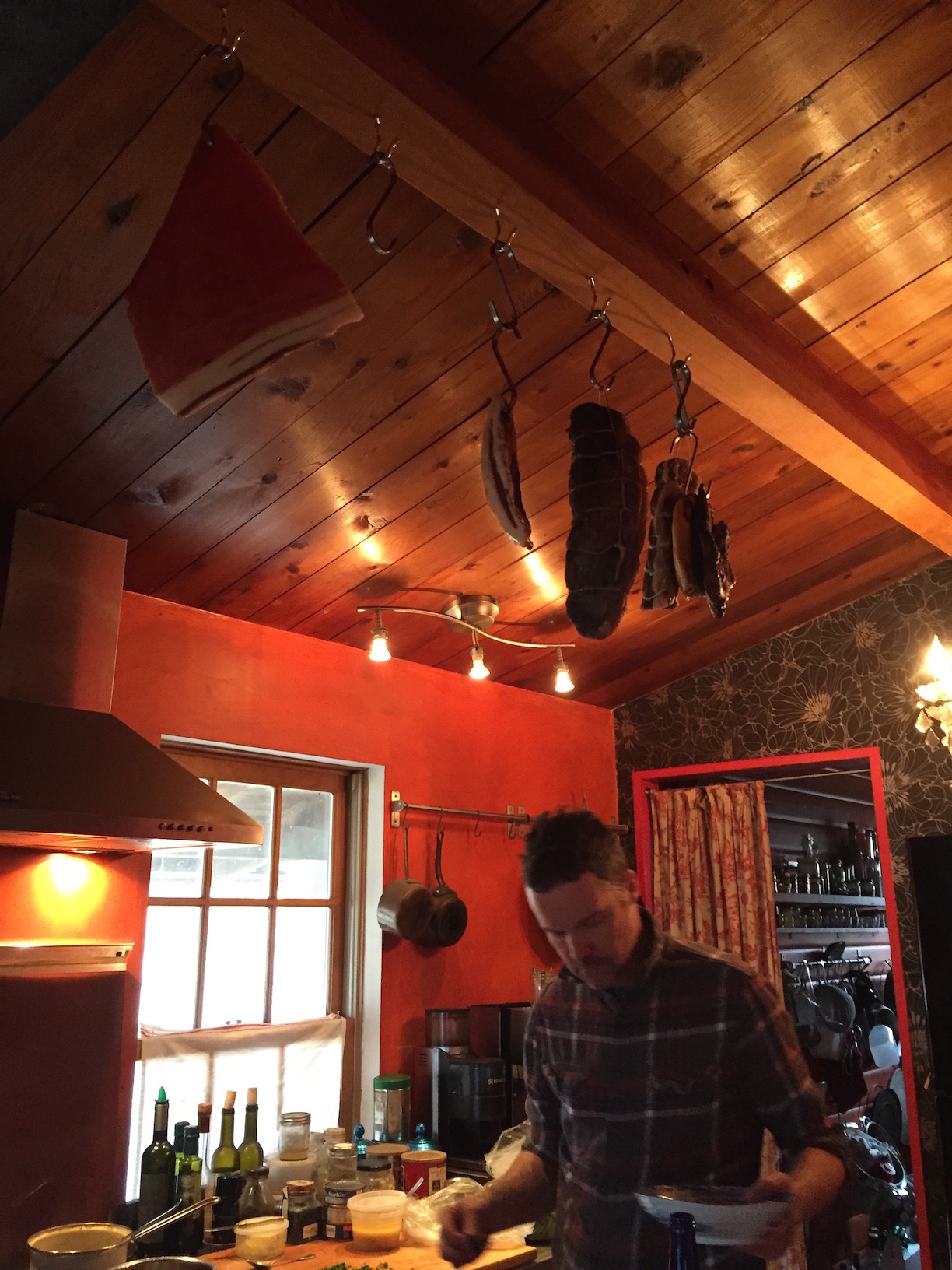 Caleb cooking in the homestead's pint-sized kitchen while meat cures overhead 